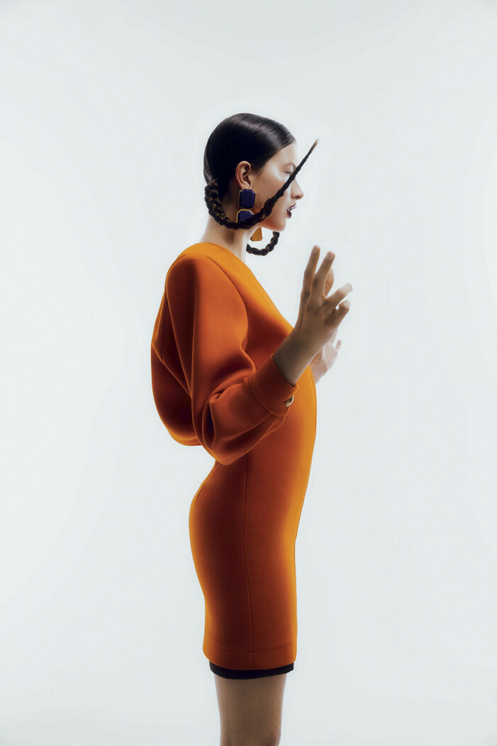 Modellen har på sig en orange klänning med puffiga ärmar.