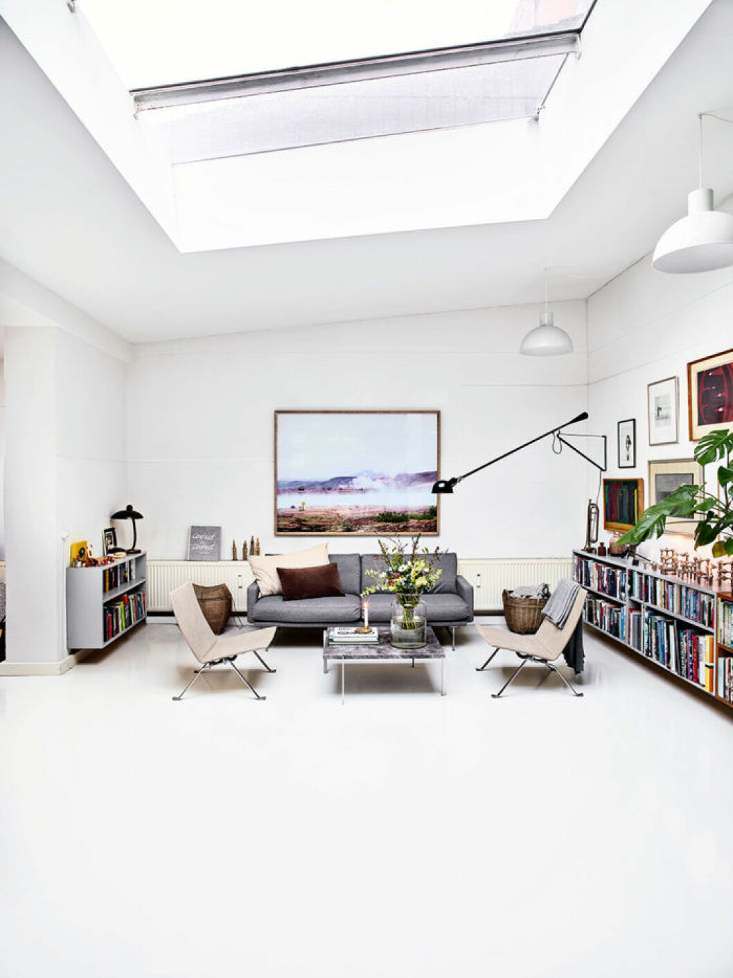 De stora takfönstren ger allrummet en nästan galleriaktig prägel. Ovan den grå Piero Lissoni-soffan hänger ett stort fotografi av Anders som togs under en semester på Island. Vägglampan 265, i design Paolo Rizzatto är med sitt industriella uttryck ett perfekt val till soffgruppen med PK22-stolar i canvas och PK61 soffbord i marmor, från Fritz Hansen.