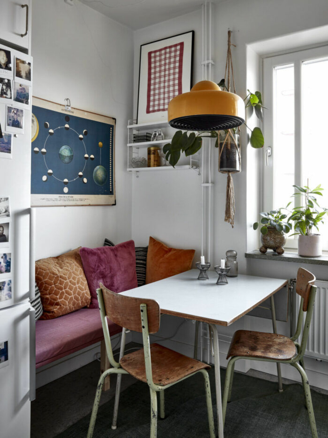 Mysig matplats i köket med färgglada textilier, orange lampa och trästolar