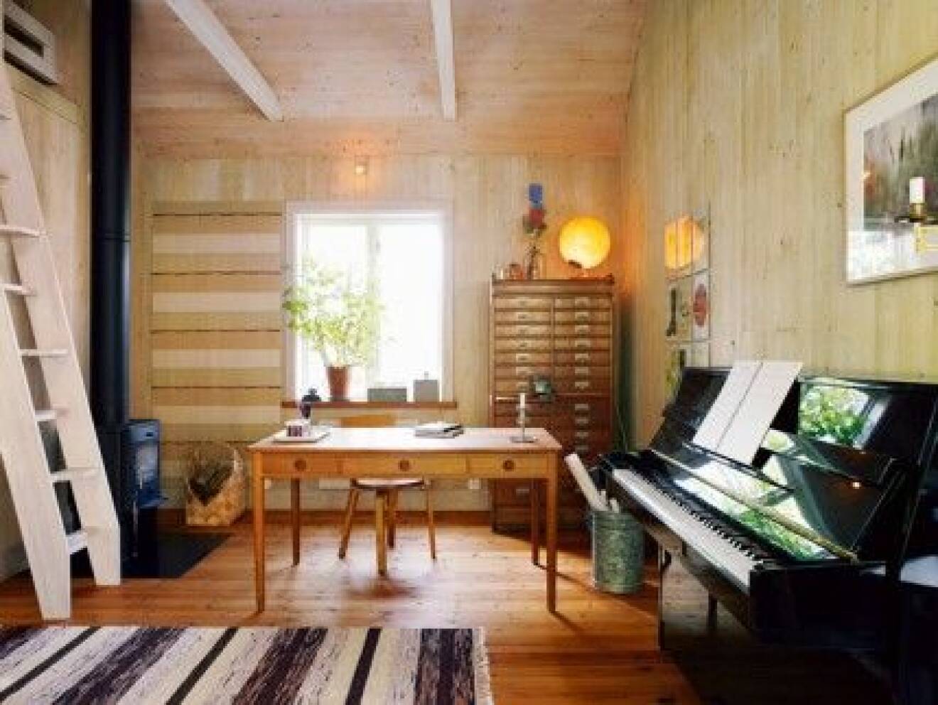  Arbets- och musikrummet har precis som sovrummet tak i nock och såväl väggar som tak är råspont som laserats ton i ton. Golvet är slipat och oljat. Tyget på väggen är hantverk i ordets rätta bemärkelse, signerat moster Edit, handvävt av växtfärgad och handspunnen ull. Tryckeriskåpet är ett loppisfynd medan skrivbordet är ritat av Hans J Wegner. Braskaminen är en Andersen 4. 