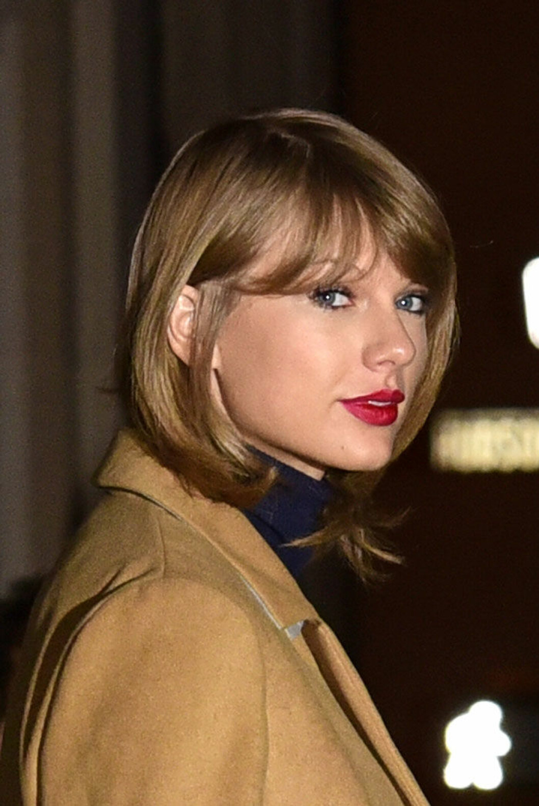 Taylor Swift med rött läppstift som enda tydliga smink. Taylor Swift med lite smink och brun kappa