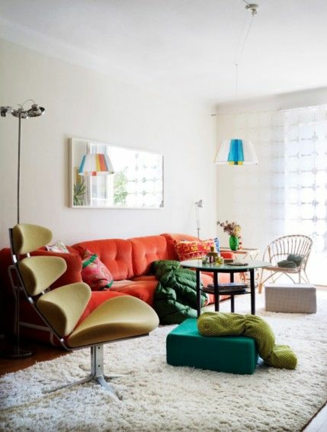 Den orangea soffan och mattan från Ikea var det enda de köpte nytt när de gjorde om efter att barnen flyttat ut. Spegeln ovanför leder in dagsljuset utifrån. På varsin sida står lampor från Ikea. Taklampan har Marie gjort av stommen till en gammal lampskärm. vardagsrum-retro-inspiration-foto-patric-johansson