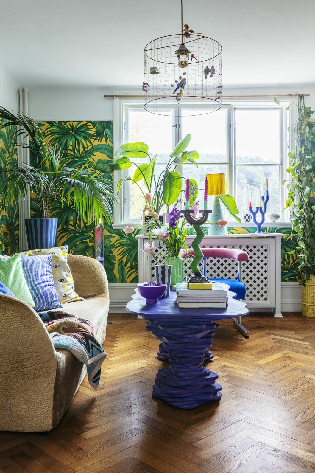 Vardagsrummet har tapetserats med en tapet från Versace, soffan är designad av Patricia Urquiola och har klätts om i ett guldfärgat sammetstyg med reptilmönster. Bordet har Viktor gjort och stolen är loppisfyndad och sedan omklädd. Accessoarerna har hittats på loppis. Djungel i vardagsrummet med tapet och gröna växter