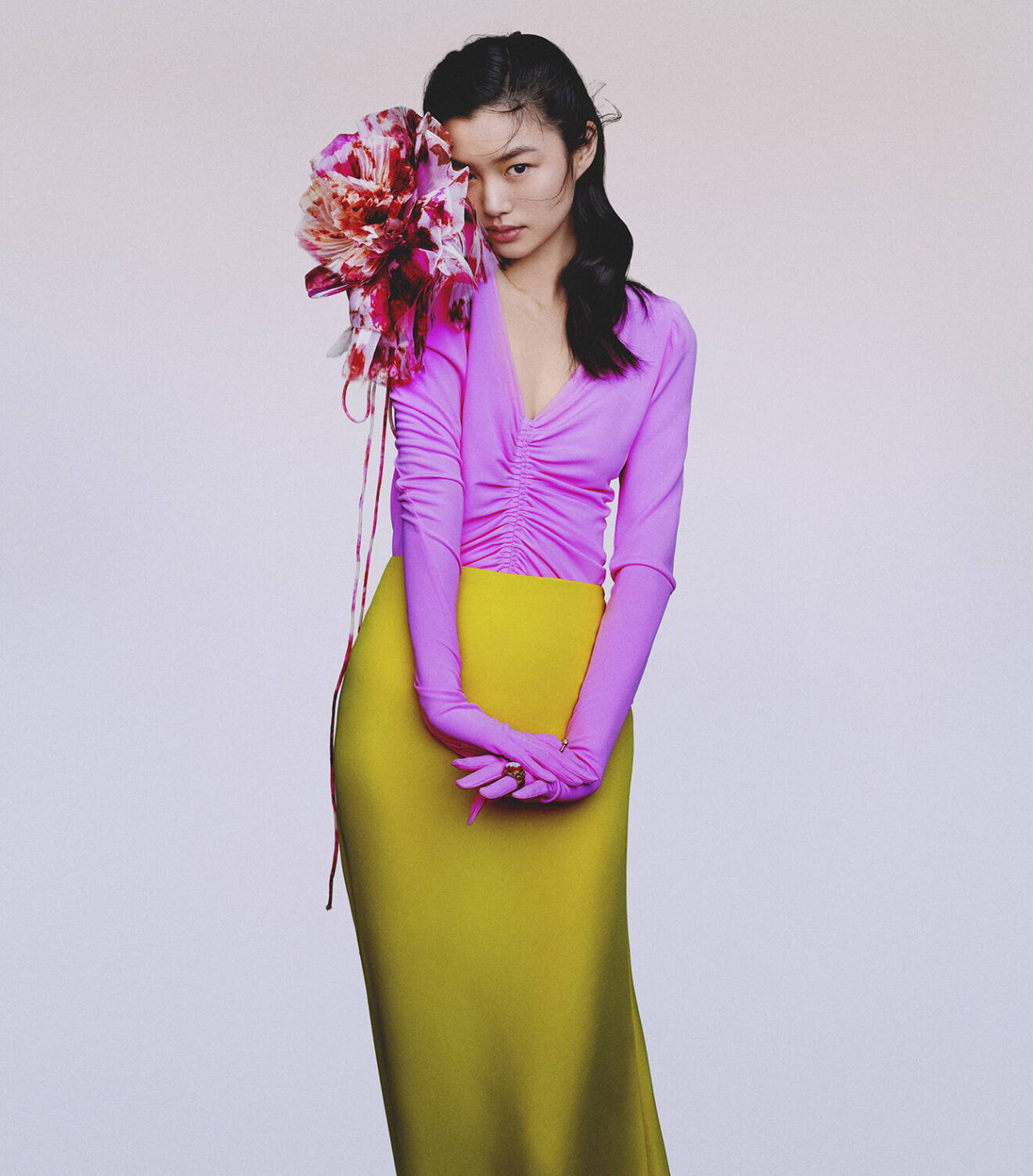 Modellen har på sig en lila topp med handskar, en gul långkjol och en stor blom-accessoar fäst på axeln