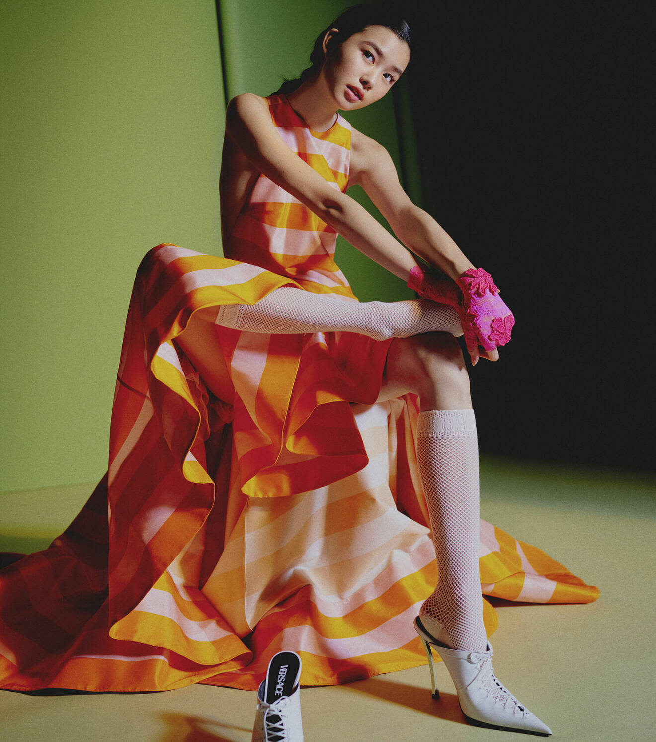 Modellen har på sig en lång randig klänning i rosa och orange tillsammans med rosa spetshandskar och vita skor